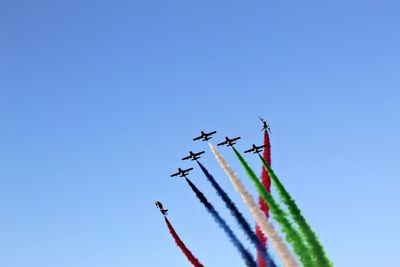 Low angle view of airplanes emitting colorful vapor trails in clear blue sky