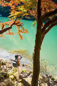 High angle view of man photographing while standing by tree at lakeshore