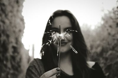 Young woman burning sparkler while standing against sky