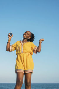 Full length of young woman standing by sea against clear sky