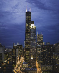 Illuminated buildings in city against cloudy sky