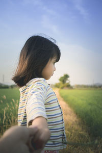 Thoughtful cute girl standing on grassy field against sky