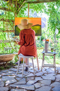 Young female artist working on her art canvas painting outdoors in her garden. 