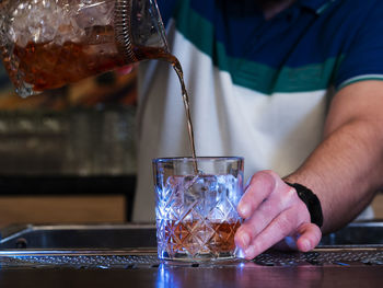 The bartender pours negroni into a glass that he holds with his hand