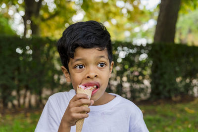 Close-up of a young boy eating ice-cream outdoors in a park.