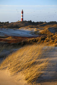 Lighthouse on beach by sea against sky