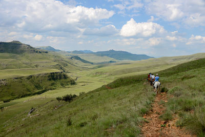 Rear view of people riding horses on mountain against cloudy sky