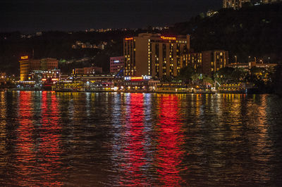 Illuminated city by river against sky at night