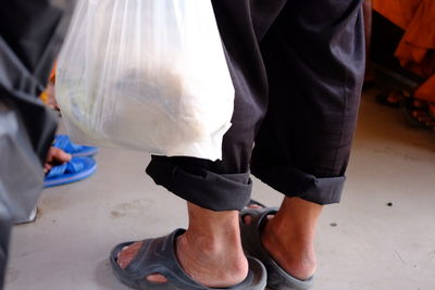 Low section of man with plastic bag standing on footpath