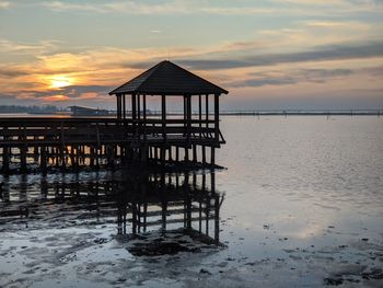 Gazebo on pier by lagoon against sky during sunset