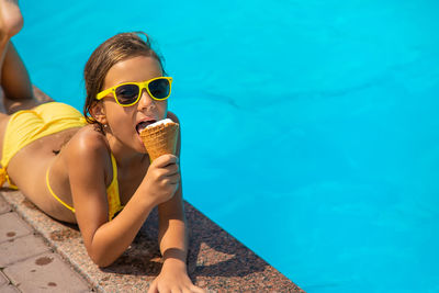 Cute girl eating ice cream lying down by swimming pool