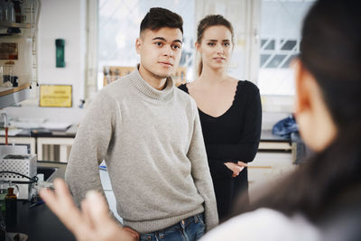 Young chemistry students looking at female teacher in laboratory