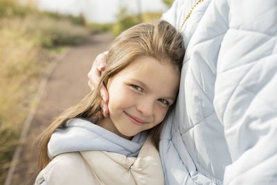 Crop mother in outerwear pressing head of cheerful daughter to chest while spending weekend day in park