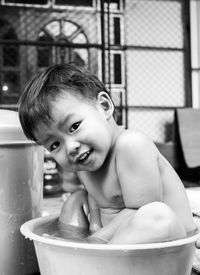 Portrait of cute boy sitting in container with water at home