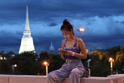 Woman sitting against illuminated city at night