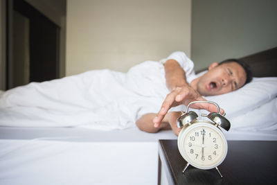 Man snoozing alarm clock on night table in bedroom