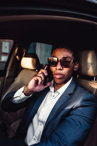 Young african american male entrepreneur in elegant formal suit talking on mobile phone while driving car on city street