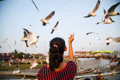 Rear view of woman flying birds against sky