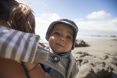 Cropped image of mother carrying son in baby carrier at beach