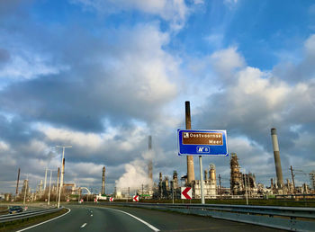 Road sign by highway against sky