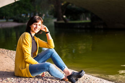 Young woman using mobile phone while sitting on lake