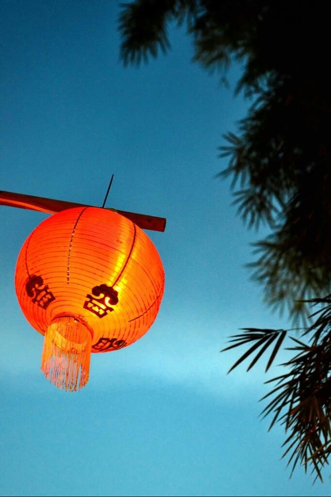 low angle view, clear sky, lantern, blue, art and craft, hanging, sky, yellow, creativity, multi colored, art, decoration, celebration, lighting equipment, copy space, chinese lantern, outdoors, cultures, illuminated, orange color