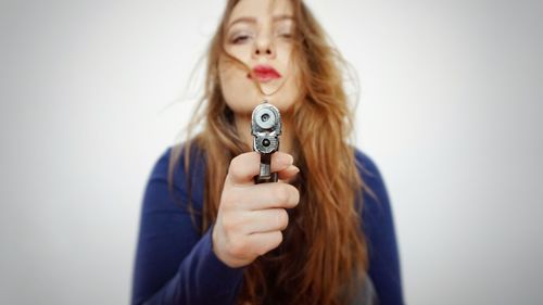 Portrait of young woman with messy hair holding handgun against white background