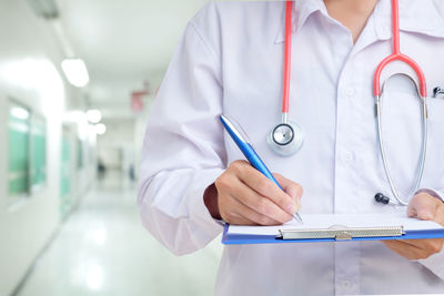 Midsection of male doctor writing on clipboard in hospital