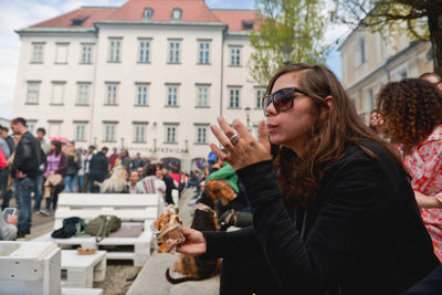 Side view of woman eating burger while sitting against building in city