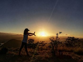 Silhouette woman standing on field against sky during sunset