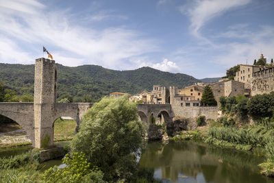 Arch bridge over river by buildings against sky