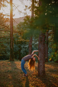 Side view of woman standing by tree in forest