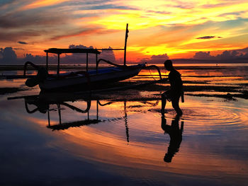 Silhouette man by boat at beach against sky during sunset