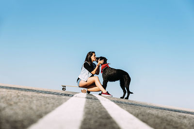 Woman with dog and skateboard against clear blue sky