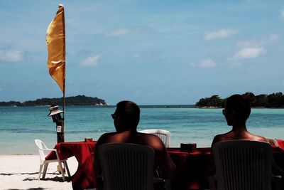 Rear view of couple sitting on chair at beach