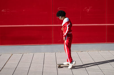 Afro-american woman with short hair and sportswear with a skateboard on red background in city