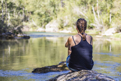 Rear view of woman sitting on rock by lake