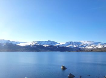 Scenic view of lake and snowcapped mountains against clear blue sky