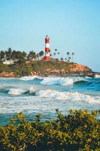Lighthouse by sea against clear sky