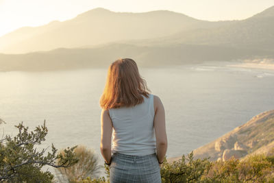 Rear view of woman standing on mountain against sky