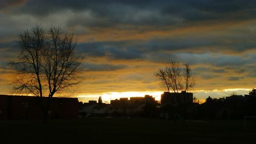 Silhouette bare trees and buildings against sky at sunset