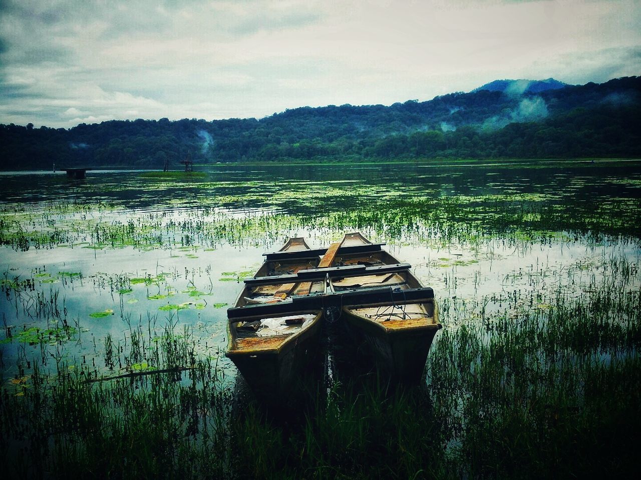 water, lake, reflection, tranquility, nature, scenics, beauty in nature, tranquil scene, sky, no people, outdoors, day, nautical vessel, abandoned, transportation, waterfront, grass, growth, mountain, moored, cloud - sky, tree, landscape