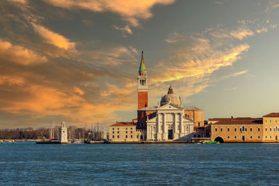 View of buildings at waterfront against cloudy sky