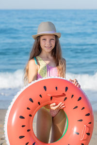 Portrait of a teenage girl with an inflatable rubber ring in a hat on the background of the sea