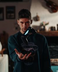 Young man holding camera while standing at home