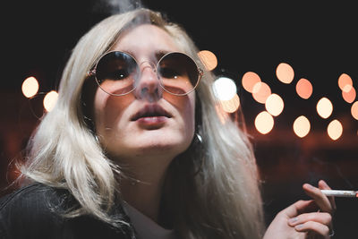 Portrait of young woman at night wearing shades, sunglasses, bokeh