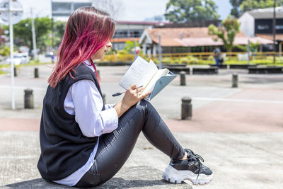 Young latina woman sitting in outdoors writing on her notepad.