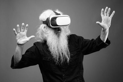 Man gesturing while wearing virtual reality simulator against gray background