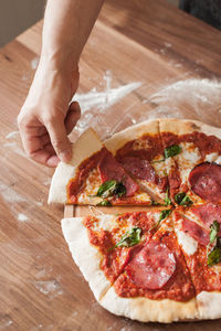 Close-up of hand holding pizza on table