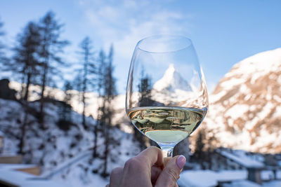 Tourist holding wineglass with view of matterhorn and snowy town against sky